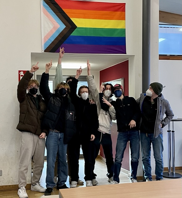 Hier sehen Sie Schüler:innen und die Progress Pride Flag.